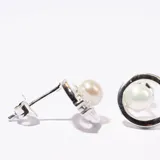 Aros plateados con forma circular, perla central y pequeños brillantes. Cierre a presión.