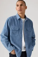 Camisa de pana color azul claro, con cuello clásico, cierre frontal de botones y dos bolsillos con solapa en el pecho.