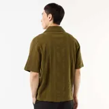 Camisa de manga corta color verde militar, con cuello solapa y cierre frontal de botones. Confeccionada en punto fantasía de algodón con sutiles rayas verticales texturizadas.
