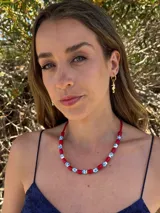 Collar corto con cuentas rojas cilíndricas y cuentas blancas con diseño floral azul. El collar está ensartado en un cordón rojo.