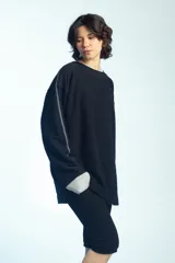 Buzo de felpa negro de corte oversize, con cuello redondo y mangas largas con puños grises doblados hacia afuera. Presenta costuras externas decorativas en tono gris claro a lo largo de las mangas y los hombros.