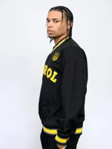 Buzo negro de nylon con cuello en V, puños y pretina con detalles en amarillo y gris. Estampado frontal con la palabra "Peñarol" en amarillo y escudo del club en la manga. Corte clásico.