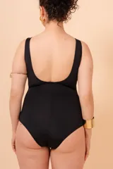 Malla entera de traje de baño, color negro, con escote en V profundo ribeteado en blanco. Presenta un cinturón blanco que se une en el centro con una argolla metálica dorada. Tiene tirantes anchos y un bolsillo interno para copa removible.