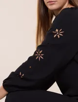 Blusa azul de corte holgado y fluido, con escote en V y mangas largas raglán que presentan detalles de calados con forma de flores y puños elastizados.