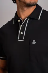 Polo de manga corta confeccionado en tejido interlock suave, color negro con detalles de vivos en color blanco en el cuello y las mangas. Presenta tapeta con botones y un bolsillo frontal con el logo bordado.