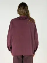 Camisa negra de corte holgado con cuello tipo bebé con volados y lazo de ajuste, cierre frontal con botones y mangas largas abullonadas con puños abotonados.