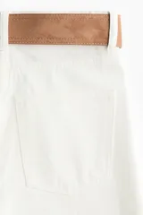 Jean de tiro alto y pierna ancha en denim de algodón blanco, con diseño de cinco bolsillos y bajo sin rematar. Incluye un cinturón de gamuza marrón con hebilla metálica.