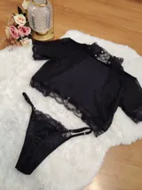 Conjunto de lencería compuesto por un top de cuello alto y una tanga, confeccionados en terciopelo negro con detalles de encaje y microtul. El top presenta mangas cortas con terminaciones en encaje y el borde inferior decorado con una cinta y encaje. La tanga es regulable y combina la textura del terciopelo con bordes de encaje.