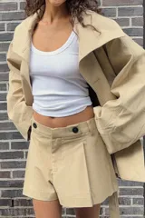Trench color beige con cuello de solapa subido y manga larga. Tiene bolsillos laterales, forro interior y cinturón de lazo en el mismo tejido. El cuello se cierra con un botón.