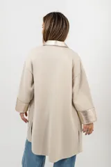 Camisa larga color beige de tejido de punto en algodón, con cuello camisero, cierre frontal con botones a presión y detalles en cuero color dorado en cuello, solapa, puños y bolsillos frontales.