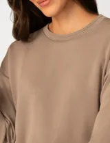 Buzo de punto suave y liviano, color beige, con cuello redondo a la base que presenta un detalle calado de crochet. De manga larga y silueta clásica con caída fluida.