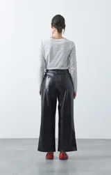Pantalón de tiro medio en símil cuero color negro, con corte flare, bolsillos laterales y costuras frontales verticales que estilizan la silueta.