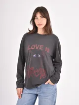 Remera de manga larga color azul piedra con efecto lavado, cuello redondo y estampa frontal con texto y diseño gráfico en tonos rojos y violetas.