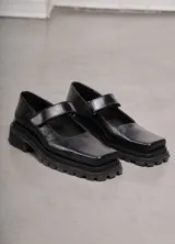 Zapato guillermina de cuero negro con punta cuadrada, tira sobre el empeine y suela track.