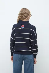 Sweater de punto azul marino con rayas horizontales blancas, cuello alto con cierre frontal y manga larga de diseño holgado.