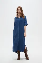 Túnica larga de viscosa azul, de corte holgado, con cuello camisero y cierre frontal de botones ocultos. Presenta mangas cortas con detalle de vuelta.