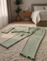 Pijama de dos piezas en color verde menta, confeccionado en tejido modal acanalado. La parte superior es una remera de manga larga con terminaciones onduladas en los puños y un pequeño bordado de corazón en el pecho. El pantalón es de corte recto con cintura elástica y cordón ajustable.