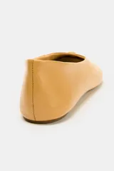 Zapato tipo bailarina plana de piel en color tostado, con pespuntes en el cuerpo, detalle metálico en la parte delantera y acabado en punta redonda.