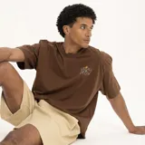 Remera marrón con estampado pequeño en el pecho que dice "We all grow" con una flor.