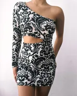 Minivestido blanco con estampado abstracto en negro, con un hombro descubierto, una manga larga y abertura en la cintura.