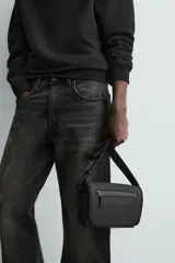 Bandolera negra con acabado engomado, compartimento principal con cierre de solapa y bolsillo con cremallera. Interior con bolsillo con cremallera. Asa de hombro ajustable.