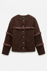 Campera de tela bouclé color marrón, con diseño de volados en tela agamuzada en el pecho y mangas. Presenta cierre frontal con botones y cuello redondo.