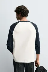 Camiseta de manga larga con estructura waffle, corte regular fit. El cuerpo es de color blanco crudo y las mangas raglán son de color azul marino. Tiene cuello redondo a contraste.