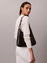 Cartera mediana Calvin Klein de poliuretano color negro, diseño estructurado tipo hobo, con correa de hombro ajustable y detalles metálicos dorados.