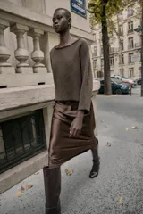 Jersey de punto color marrón con cuello barco y manga larga. Presenta pespuntes decorativos en color negro a contraste en el cuello, puños y bajo.