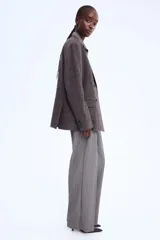 Pantalón sastrero de corte ancho y tiro alto, color gris oscuro con finas rayas verticales blancas (pinstripe). Presenta pliegues frontales (pinzas) y pretina con cierre oculto.