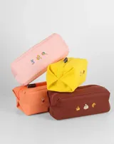 Neceser rectangular de tela color ladrillo con cierre superior y tres bordados pequeños: una hoja de arce, una taza de té y un croissant.