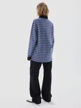 Chomba de manga larga con diseño a rayas horizontales en tonos azul y gris. Presenta cuello polo y cartera de botones en color negro, con puños negros y bordado pequeño en el pecho.