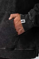 Buzo canguro con capucha, de calce oversize y efecto lavado gastado. Presenta un estampado gráfico central en color blanco y un pequeño parche con logo en el puño.