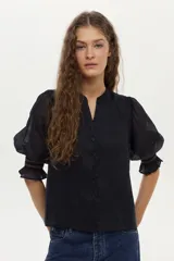 Blusa color tostado confeccionada en lino, con mangas abullonadas de ramie y detalles de bordado en punto smock en los puños.