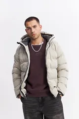 Campera puffer con capucha, diseño acolchado, cierre frontal y bolsillos laterales. Presenta un interior en contraste de color verde oliva.