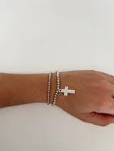 Set de dos pulseras plateadas elásticas con cuentas redondas y dije circular con una cruz calada.