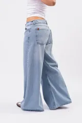 Jeans wide leg de denim rígido en lavado celeste vintage, con diseño de cintura cruzada y cierre asimétrico de doble botón.
