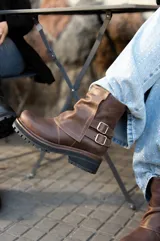 Bota de cuero marrón con caña arrugada, hebillas doradas y suela track.