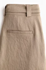 Pantalón de tiro alto con corte holgado y piernas amplias, color marrón, con pliegues delanteros y cinturón del mismo tejido con hebilla circular.