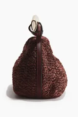 Bolso de mano de textura rugosa color bordó, con asa rígida de metal dorado de diseño ondulado y cierre magnético.