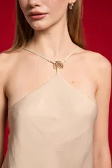 Top de poliéster color beige, con diseño holgado, cuello halter y detalle de aplicación metálica en el escote.
