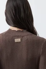 Polera de tejido de punto con textura calada y diseño de líneas verticales acanaladas. Presenta cuello alto y mangas largas con puños delicados, de silueta entallada.