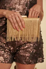 Clutch rígido de color dorado con acabado metalizado y flecos colgantes en la parte frontal. Cuenta con cierre de broche metálico en la parte superior.