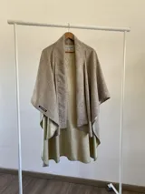 Ruana de diseño estructurado confeccionada en tela tipo tapiz, con solapas amplias y caída fluida. Presenta un tono neutro con textura sutil y acabado reversible en un tono más claro.