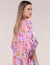 Kimono de gasa ligera con estampado floral en tonos rosados, anaranjados y violetas. Presenta diseño abierto al frente, mangas amplias tipo kimono y detalle de borlas en el ruedo asimétrico.