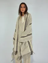 Ruana tipo pashmina color tostado con diseño a cuadros y rayas en tonos beige y marrón. Presenta flecos en los bordes.