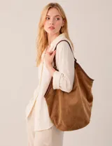 Cartera tipo hobo de gran capacidad confeccionada en símil gamuza color marrón. Presenta un diseño relajado con ribetes de cuero sintético a tono en los bordes y una asa de hombro integrada. Cuenta con un compartimento interior independiente y un diseño minimalista.