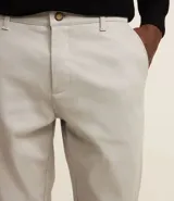 Pantalón de vestir para hombre, color beige claro, de corte slim y sastrería. Presenta cierre frontal con botón y cremallera, y bolsillos laterales y traseros.