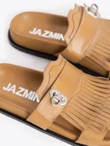 Sandalias planas color tostado de cuero vacuno, con capellada adornada con flecos y una tira con hebilla metálica.