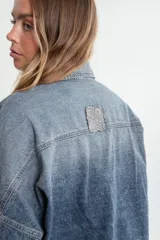 Campera de denim azul con calce boxy, cuello clásico, cierre con botones metálicos, mangas largas con puños abotonados, dos bolsillos frontales con solapa y parche con logo en el frente.